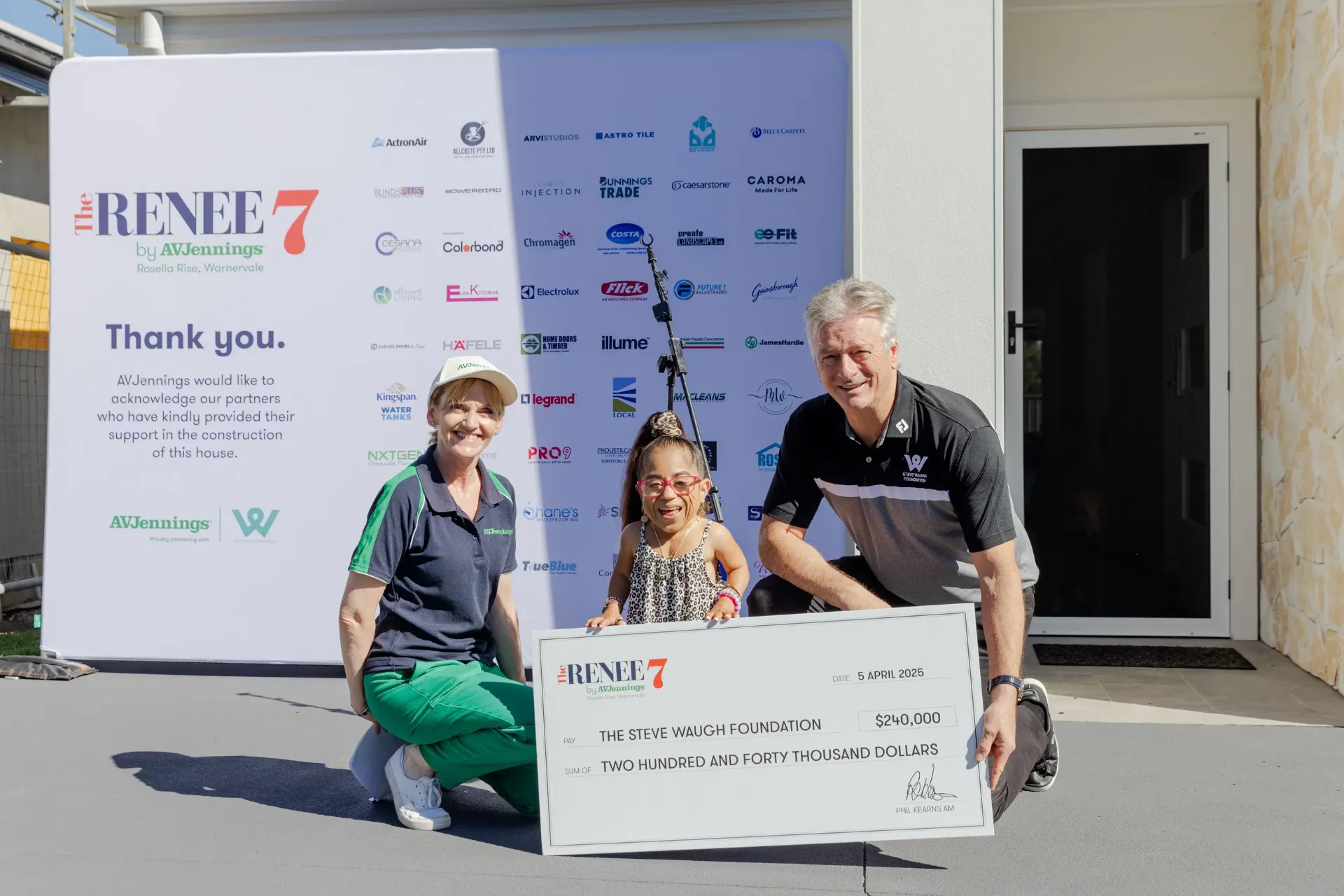 Three people pose outside: a woman, a girl in a wheelchair, and a man, all smiling and holding a large $240,000 check made out to The Steve Waugh Foundation. A sponsor banner is displayed in the background.